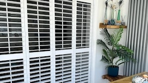 Un comedor con mesa y sillas de madera, una planta en maceta y un estante con objetos decorativos.