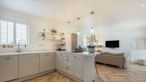 Una cocina moderna con armarios blancos, piso de madera en espiga e iluminación colgante.