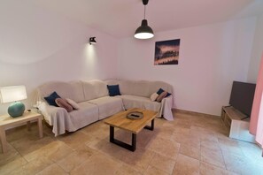 Uma sala de estar com sofá bege, mesa de centro de madeira, luminária e televisão em um suporte.