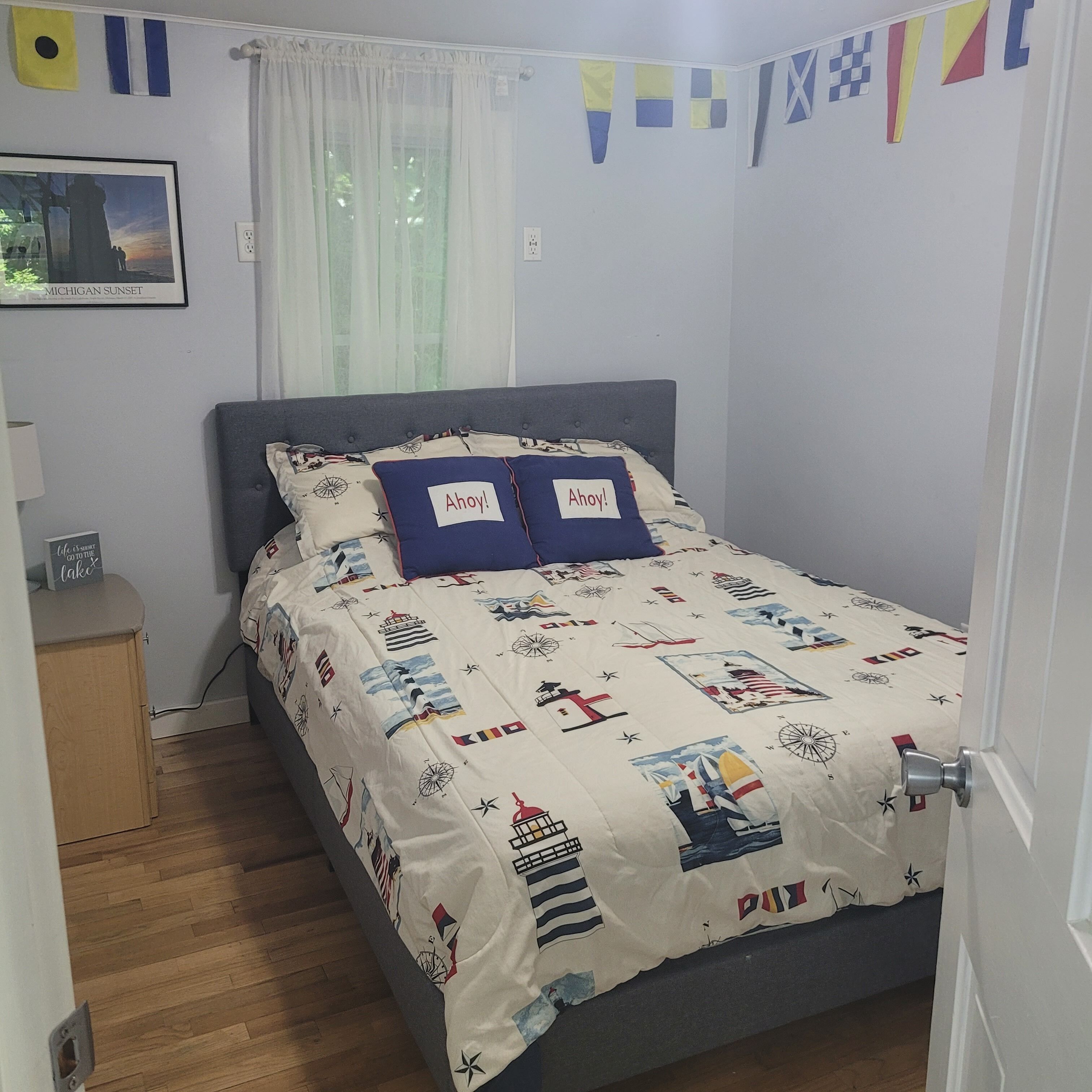 Een slaapkamer met een bed, een nachtkastje, een raam met gordijnen en een aan de muur hangend schilderij.