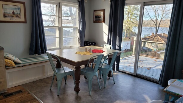 A dining area with a table, chairs, and a view of a backyard through large windows. - Country cottage, Baseline Lake . Come fish, kayak or enjoy a camp fire.  (Gobles)