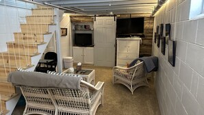 A compact living space with a staircase, wicker furniture, a television, and a small kitchen area. - Country cottage, Baseline Lake . Come fish, kayak or enjoy a camp fire.  (Gobles)
