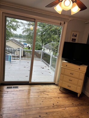 A room with a sliding glass door leading to a deck, a television on a cabinet, and a ceiling fan. - Country cottage, Baseline Lake . Come fish, kayak or enjoy a camp fire. (Gobles)