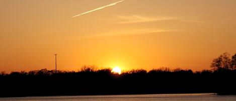 A sunset over a calm body of water with a silhouette of trees and a distant light pole.