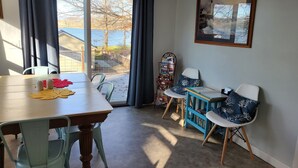 A dining area with a table, chairs, and a view of a lake through a glass door. - Country cottage, Baseline Lake . Come fish, kayak or enjoy a camp fire.  (Gobles)