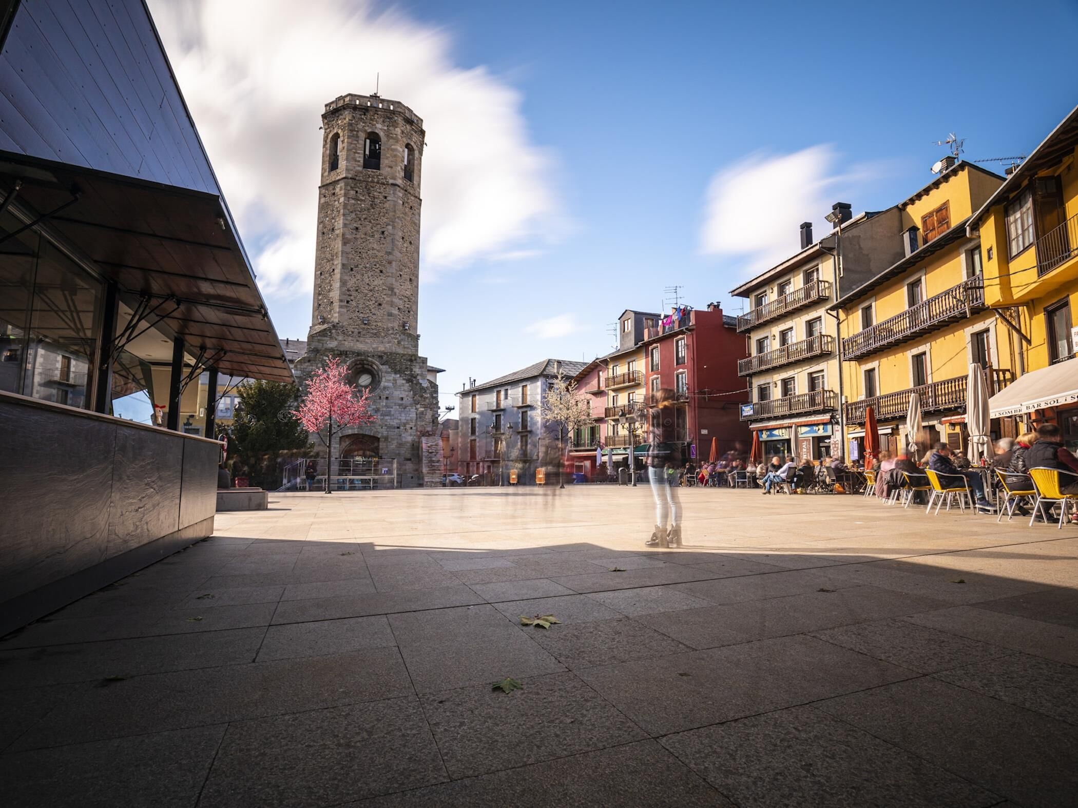 Una plaça amb una torre històrica, edificis moderns i zones d'aigües obertes.