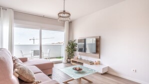 A modern living room with a sofa, a glass coffee table, a TV, and a balcony with a view of the sea. - Stunning Apartment in Estepona, Spain Private Pool (Estepona)