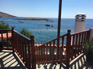 A coastal view from a balcony with a wooden railing, overlooking the sea and boats.