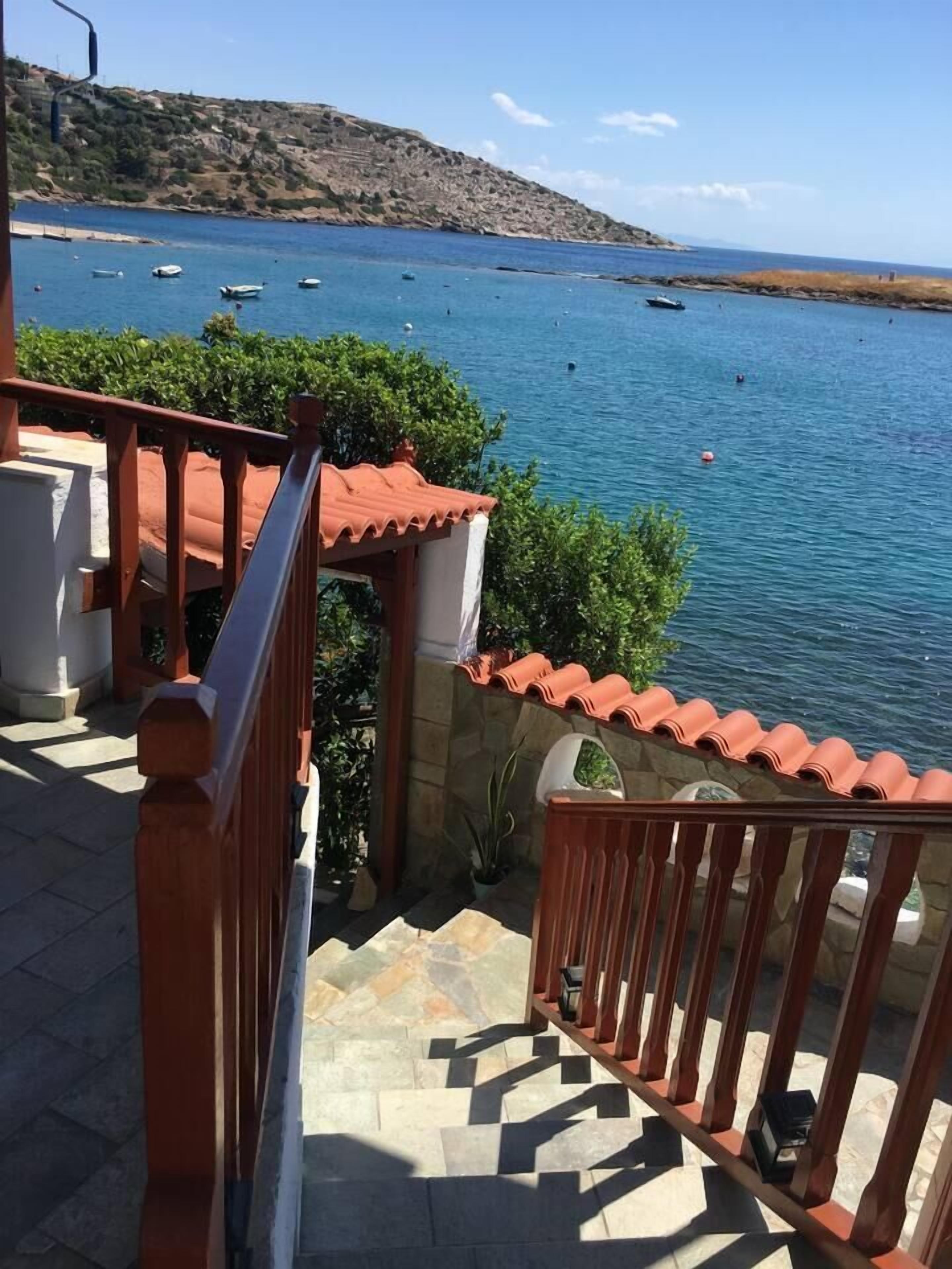Eine Treppe führt zu einem Balkon mit Blick auf eine Küstenlandschaft, auf der Boote liegen.