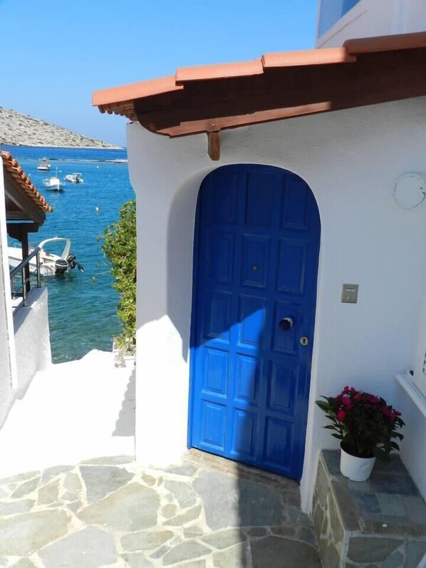 A blue door with a white wall and stone flooring, leading to a balcony overlooking a marina with boats.