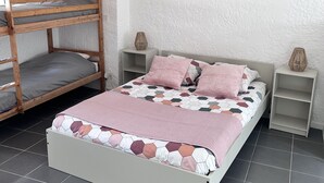 A bedroom with a bunk bed, a single bed with a patterned bedspread, bedside tables, and a tiled floor. - Apartment (Riez)