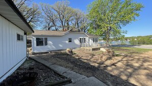 A white mobile home with a deck and a small porch, surrounded by trees and a lake view. - Lake view home on 1.3 acres, lake access 1 block away.
Camper parking available. (Spirit Lake)