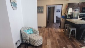 A spacious living area with a wooden floor, a patterned armchair, a dining area with a kitchen in the background, and a door leading to another room. - Lake view home on 1.3 acres, lake access 1 block away.
Camper parking available. (Spirit Lake)