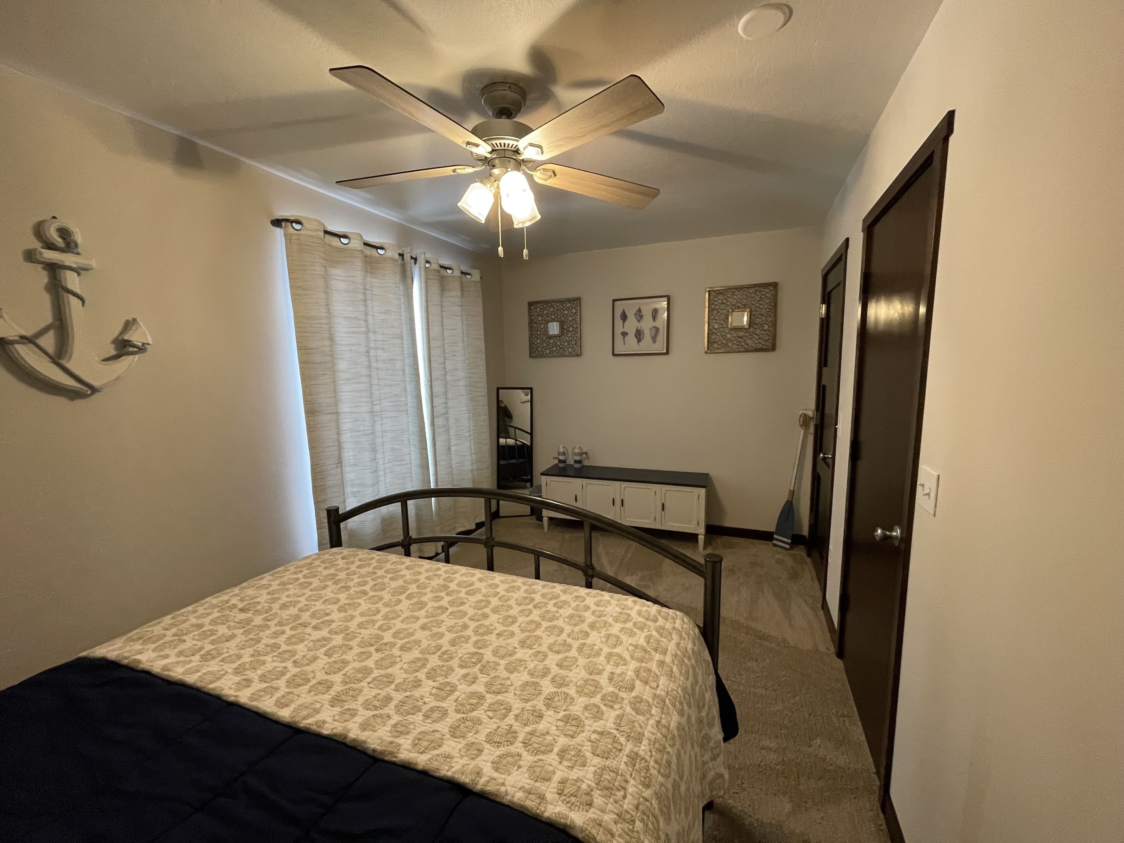 A bedroom with a bed, a ceiling fan, a dresser, and a door.