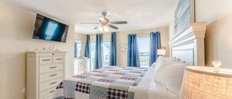 Quarto com cama, cómoda, televisão, ventoinha no teto e janela com cortinas.