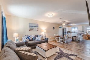A modern living room with a sofa, coffee table, and dining area. There is a kitchen in the background with a refrigerator and cabinets. - Cozy 2bed/1.5bath beach townhome!! 75 steps to the beach! Stunning ocean view! (Port St. Joe)