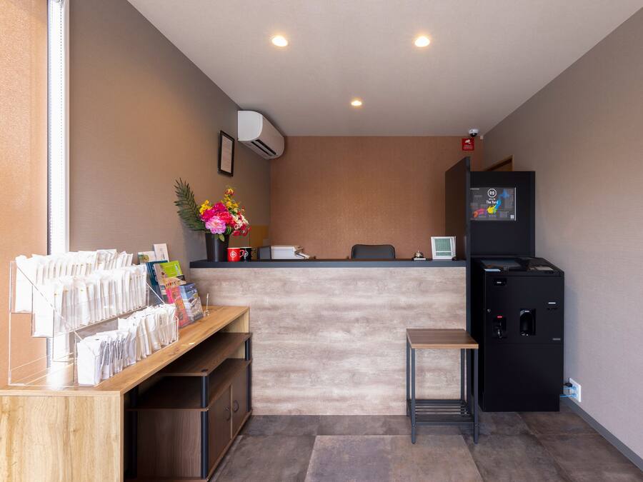 A reception area with a wooden desk, a small table, a refrigerator, and a wall-mounted air conditioner.