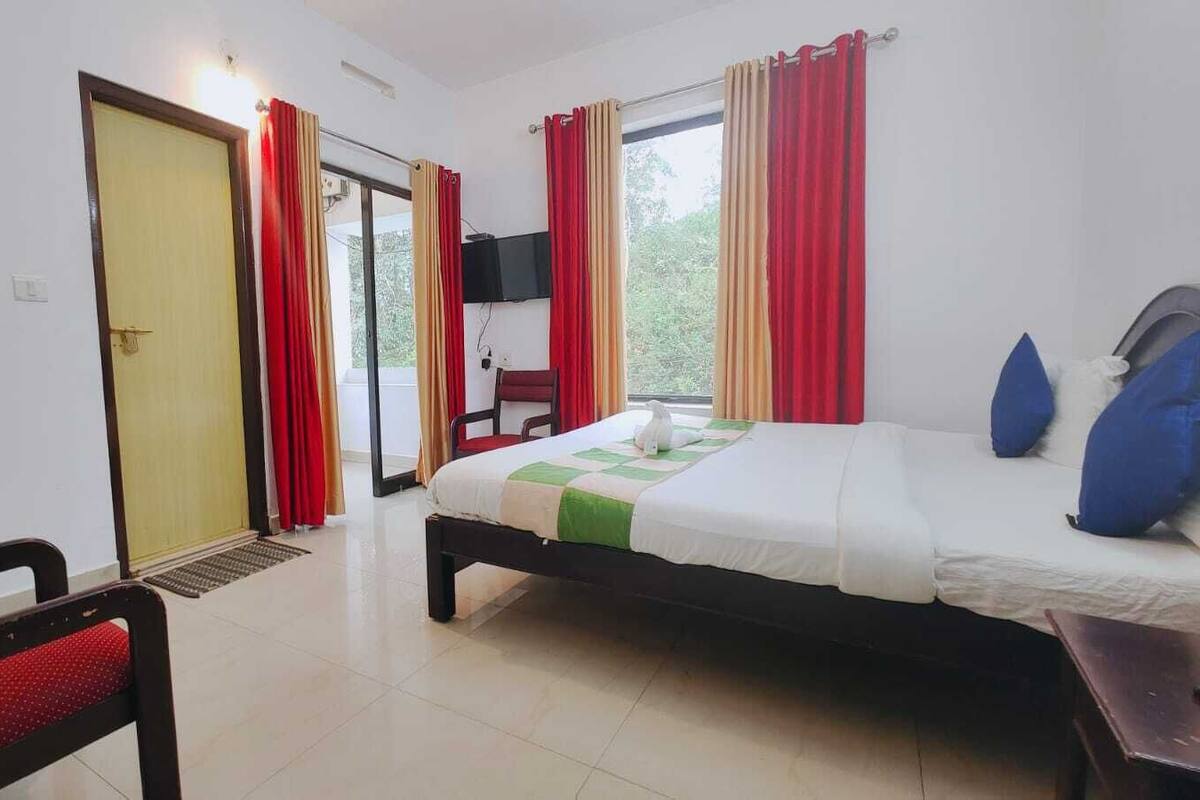 A hotel room with a bed, a chair, a TV, and a window with curtains.