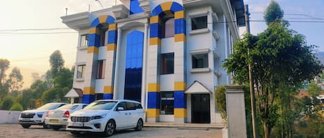 A building with a modern architectural style, featuring a prominent entrance with a blue and yellow color scheme. There are three white cars parked in front of the building.