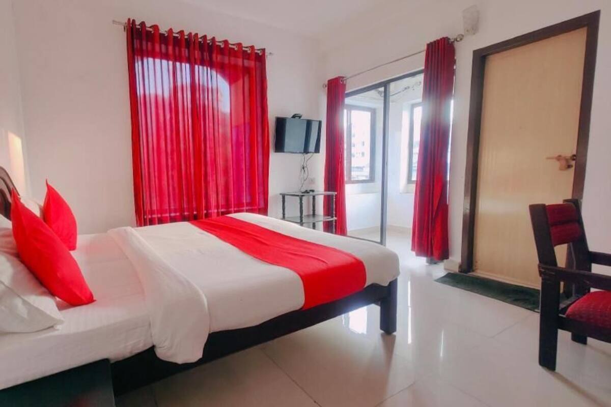 A hotel room with a bed, red curtains, a TV, and a door.