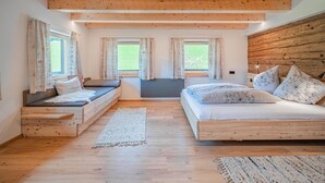 A bedroom with a wooden ceiling, two windows with curtains, a bed with patterned pillows, and a small seating area with a bench. - Holiday home a short distance from the ski lift (Hopfgarten im Brixental)