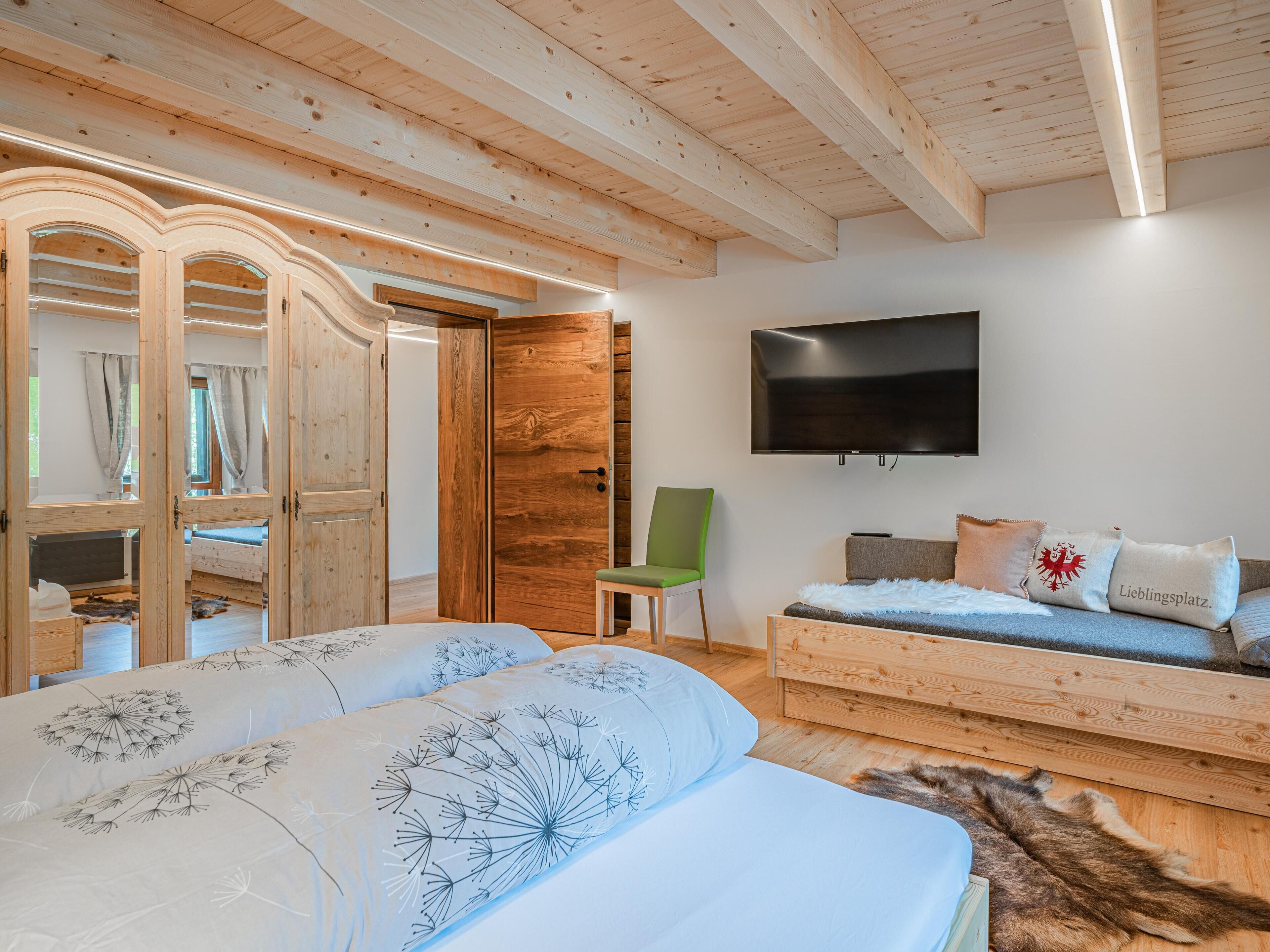 Une chambre à coucher avec un lit, un fauteuil vert, une télévision et des meubles en bois.