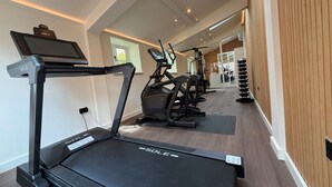 A modern gym with treadmills, stationary bikes, and a wall-mounted TV. - Estate Lodge -  Luxury Cottages (Leominster)