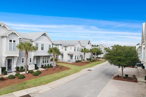 A row of white townhouses with a well-maintained lawn and palm trees.