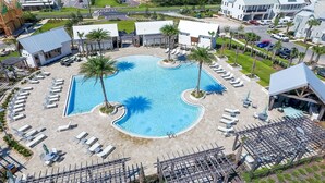 A resort with a central swimming pool, sun loungers, and a view of the ocean.