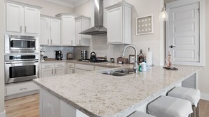 A modern kitchen with white cabinets, stainless steel appliances, a granite countertop, and a large island with bar stools.