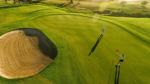 Een golfbaan met een zandbunker, een putting green en een waterhindernis.