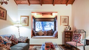 Un salon chaleureux avec un canapé, une table basse en verre, un meuble en bois et un coin fenêtre agrémenté de coussins.