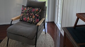 A cozy room with a grey armchair, a black floor lamp, and a framed bird artwork on the wall.
