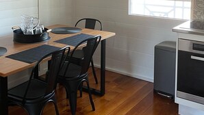 A compact kitchen with a wooden table, black chairs, and pendant lights. A clock and window with blinds are visible.