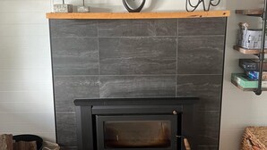 A modern fireplace with a black tiled surround, a wooden mantel, and decorative items including pinecones and a heart-shaped sign.