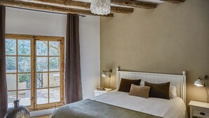 A bedroom with a large bed, a nightstand, a lamp, and a view through a window.