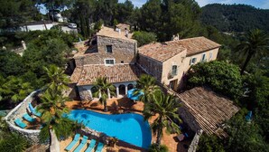 A large villa with a swimming pool surrounded by palm trees and a stone wall.