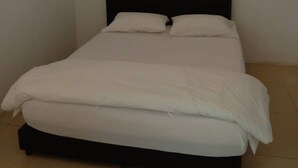 A single bed with a black headboard in a room with plain white walls and a tiled floor.