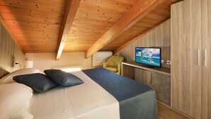 Une chambre à coucher avec un lit, des oreillers, un téléviseur posé sur un meuble et des murs en bois.
