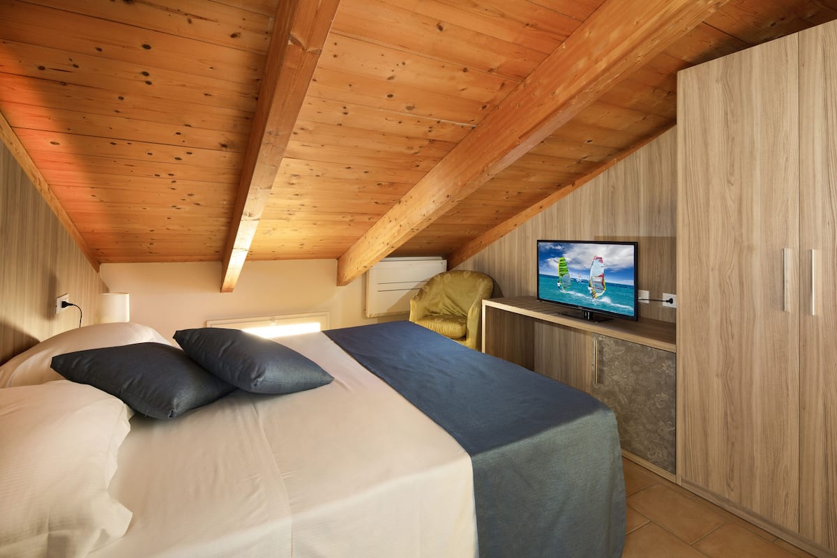 A bedroom with a bed, pillows, a television on a stand, and wooden walls.