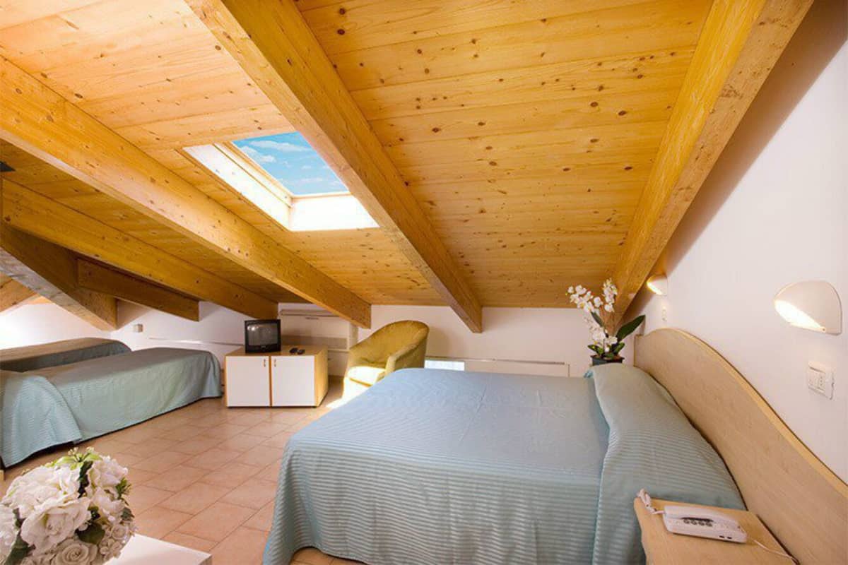 A bedroom with a skylight, a bed, a bedside table, a chair, and a small desk.