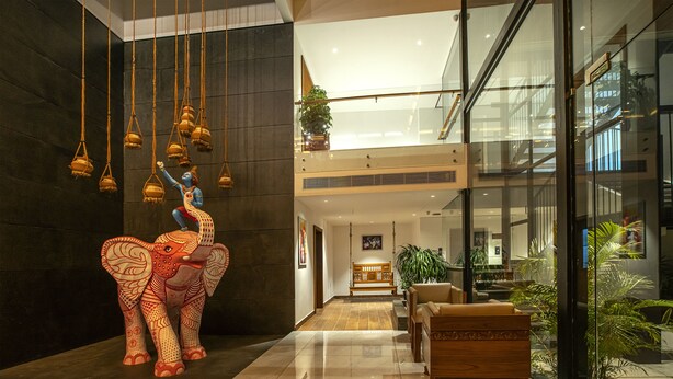 Un hall d’entrée orné d’une grande sculpture d’éléphant, avec un banc en bois et un mur de verre donnant sur un bâtiment moderne.