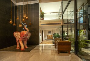 A lobby with a large elephant sculpture, a wooden bench, and a glass wall overlooking a modern building.