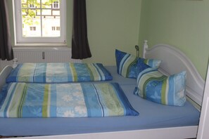 A bed with blue and green floral bedding, a window with curtains, and a view of buildings outside.