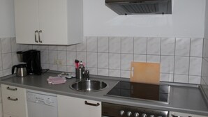 Cozinha com armários brancos, pia de aço inoxidável, cafeteira e forno embutido.