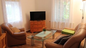 Sala de estar com dois sofás de couro, uma mesa de centro de vidro, um armário de madeira com uma televisão de tela plana e cortinas leves.