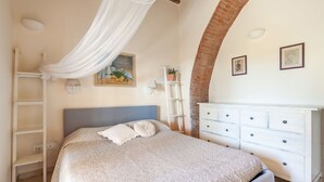 A bedroom with a bed, a white dresser, a ladder, and a painting on the wall. - Belvilla by OYO Casa Cecina (Riparbella)