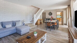 Una sala moderna con un sofá seccional gris, una mesa de centro de madera, y una escalera que lleva a un comedor con una mesa y sillas de madera.