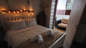Een net opgemaakt bed met witte lakens en een bruine plaid, een nachtkastje met een vaas, en een lichtslingering boven het bed.