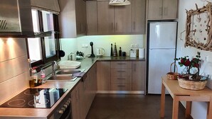 Een moderne keuken met houten kastjes, een roestvrijstalen fornuis en een inbouwoven. Er is een koelkast, een spoelbak en een tafel met een bloevas.